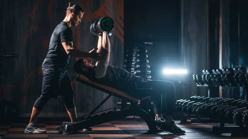 Junger Mann trainiert mit Personal Trainer im modernen Fitnessstudio