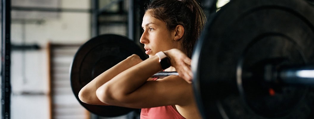 Sportliche Frau beim Krafttraining mit der Langhantel im Fitnessstudio.